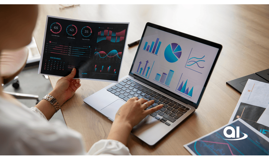 Person analyzes data on a laptop and in printed reports with charts and graphs on a wooden table.